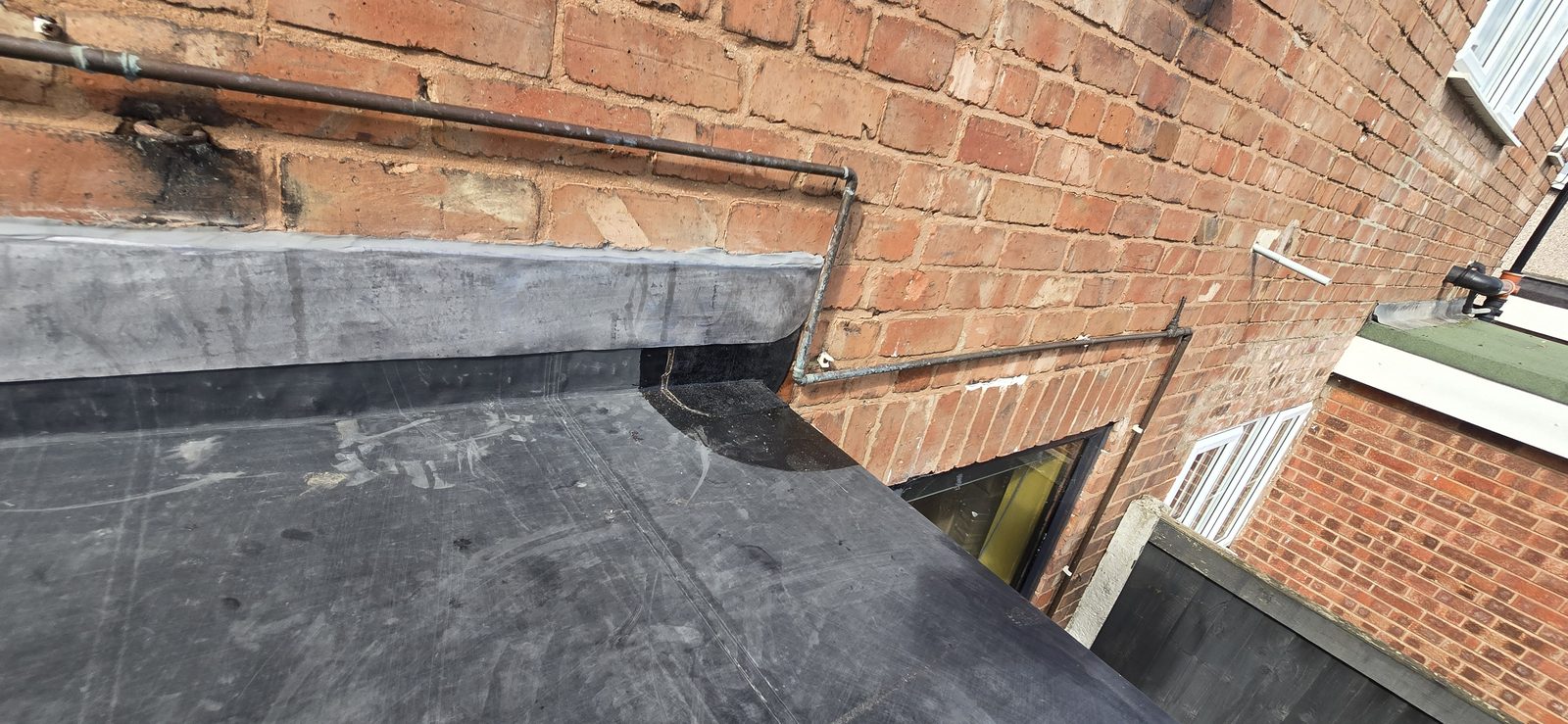 Completed EPDM rubber flat roof seen across the roof towards the house wall and lead flashing