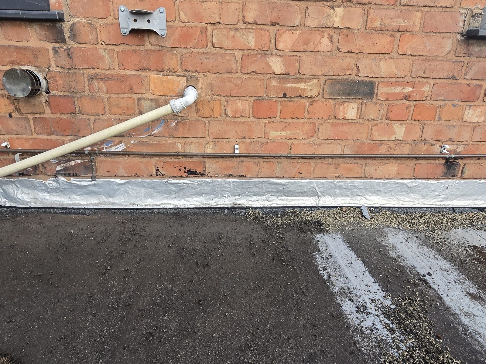 Self-adhesive flashing tape stuck to the brickwork where the old flat roof met the house wall